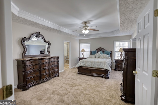 carpeted bedroom with ceiling fan, multiple windows, a tray ceiling, and ensuite bathroom