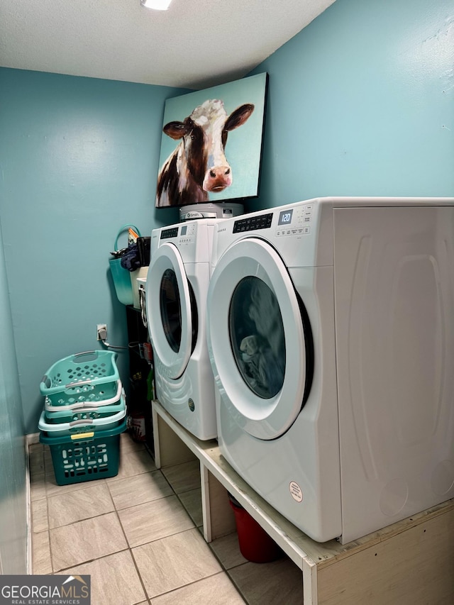 laundry room featuring a textured ceiling, light tile patterned flooring, and washer and clothes dryer