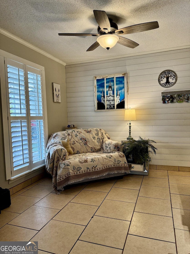 living room featuring wooden walls, ceiling fan, tile patterned flooring, a textured ceiling, and ornamental molding