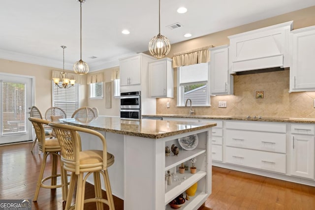 kitchen with light stone counters, pendant lighting, white cabinets, and a center island