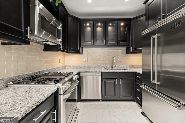 kitchen with marble finish floor, dark cabinetry, a sink, glass insert cabinets, and appliances with stainless steel finishes
