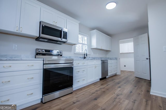 kitchen with stainless steel appliances, light wood-type flooring, light stone countertops, white cabinets, and sink