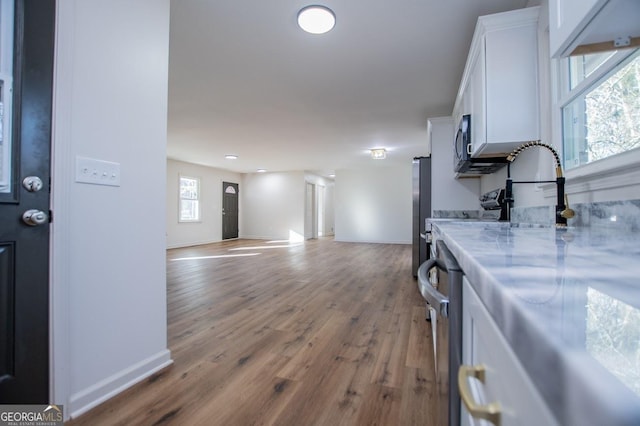 kitchen with hardwood / wood-style flooring, appliances with stainless steel finishes, white cabinets, light stone counters, and sink