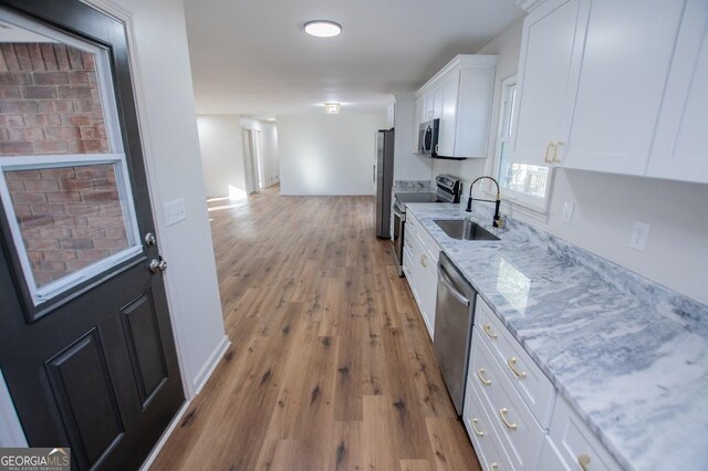 kitchen with white cabinetry, stainless steel appliances, light wood-type flooring, light stone countertops, and sink