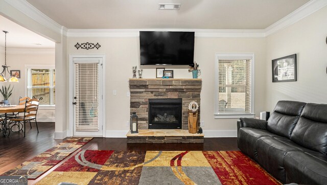 living room with crown molding, dark wood-type flooring, a stone fireplace, and ceiling fan