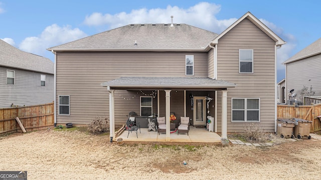 rear view of property featuring a shingled roof, fence, and a patio