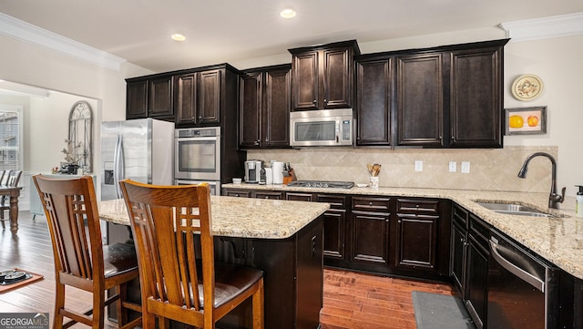 kitchen with ornamental molding, stainless steel appliances, light wood-style floors, a kitchen bar, and a sink