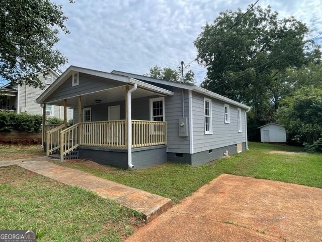 view of front of home with a front yard, covered porch, and a storage shed