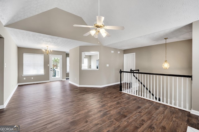 empty room featuring lofted ceiling, dark wood-type flooring, ceiling fan with notable chandelier, and a textured ceiling