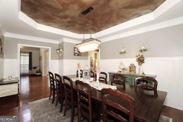 dining area with dark wood-type flooring, ornamental molding, and a raised ceiling