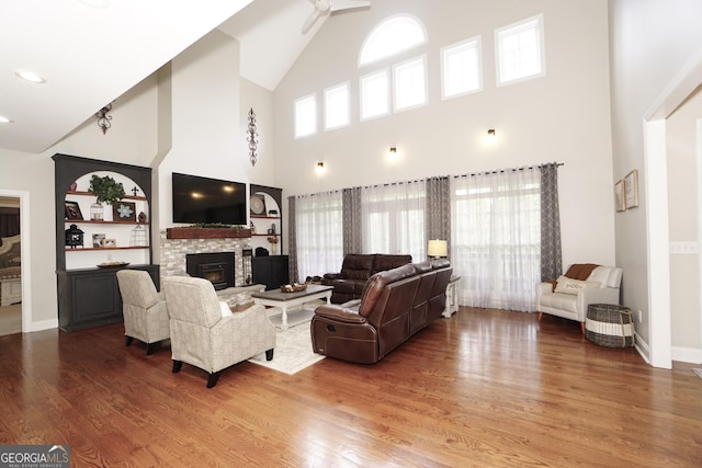 living room featuring a high ceiling, hardwood / wood-style floors, built in shelves, and a stone fireplace