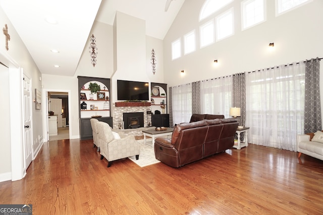 living room featuring a fireplace, built in features, a high ceiling, and hardwood / wood-style flooring