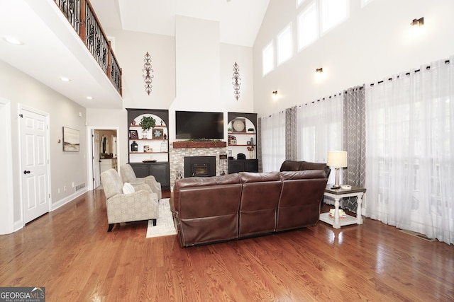 living room with hardwood / wood-style flooring, built in features, a stone fireplace, and a towering ceiling