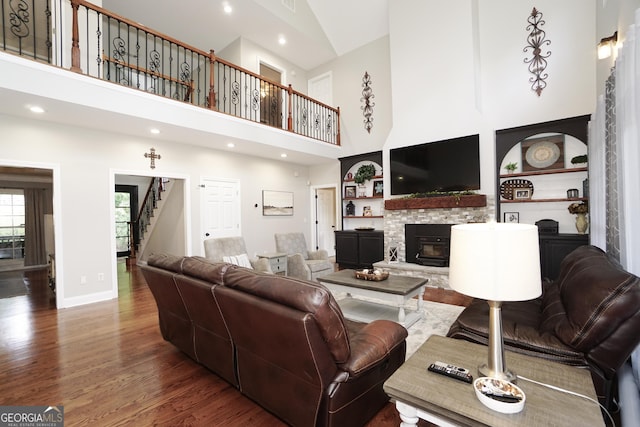 living room with built in features, a high ceiling, a stone fireplace, and dark hardwood / wood-style floors