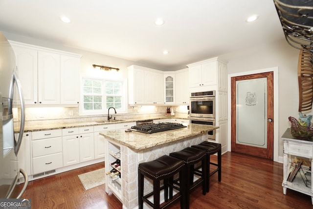 kitchen with white cabinets, appliances with stainless steel finishes, a kitchen island, sink, and light stone counters