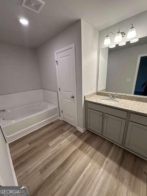 bathroom with hardwood / wood-style flooring, a washtub, and vanity