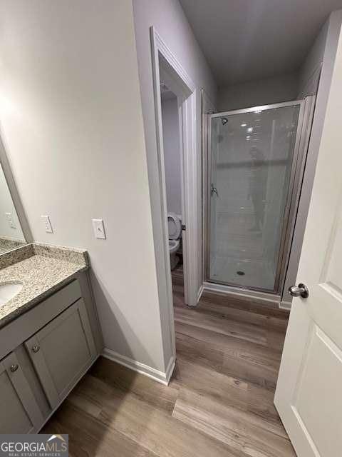 bathroom featuring toilet, walk in shower, hardwood / wood-style flooring, and vanity