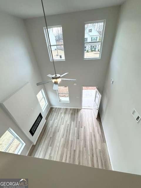 unfurnished living room with ceiling fan, a high ceiling, light wood-type flooring, and a healthy amount of sunlight