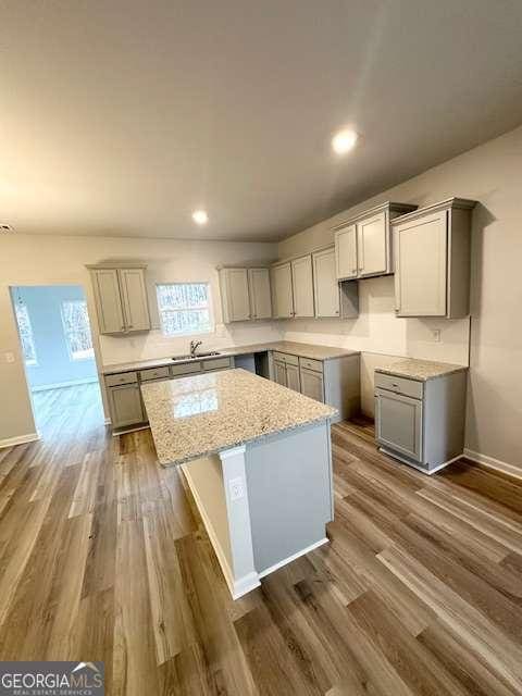 kitchen with light stone countertops, dark hardwood / wood-style floors, gray cabinets, and a kitchen island