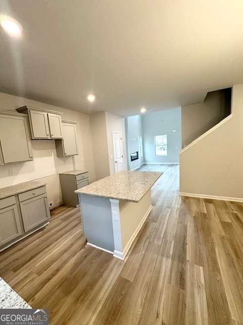 kitchen with light stone counters, gray cabinets, a center island, and light wood-type flooring