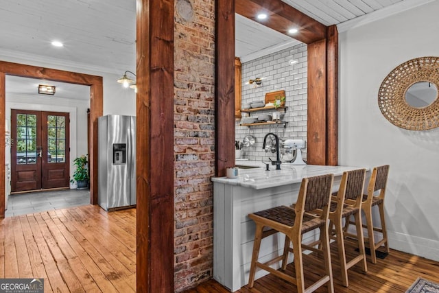 bar featuring sink, crown molding, light hardwood / wood-style flooring, stainless steel refrigerator with ice dispenser, and french doors