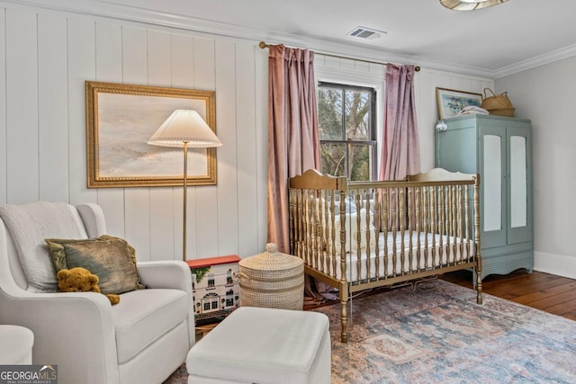 bedroom with ornamental molding, wood-type flooring, and a crib