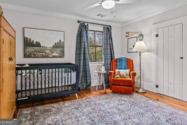 bedroom featuring dark wood-type flooring, a crib, ornamental molding, and ceiling fan