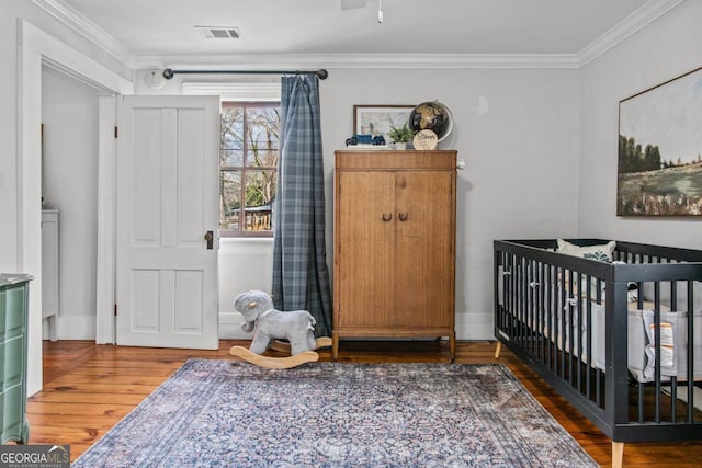 bedroom with crown molding, a nursery area, and dark wood-type flooring