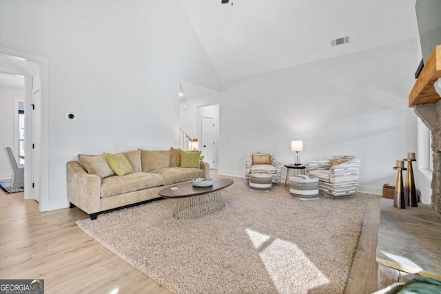 living room featuring wood finished floors, baseboards, visible vents, high vaulted ceiling, and stairs