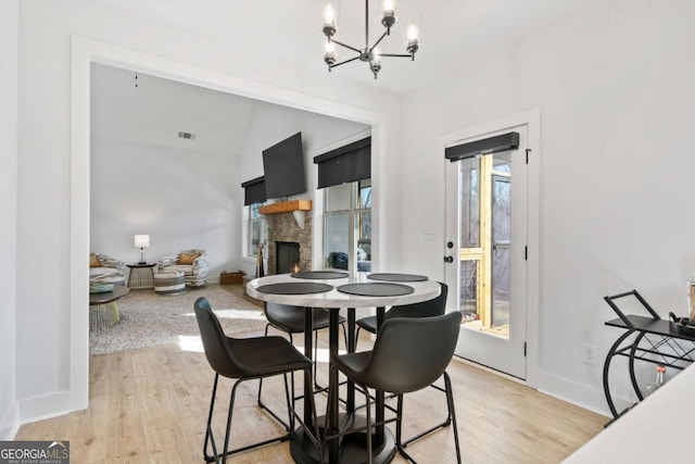 dining space featuring a chandelier, baseboards, a stone fireplace, and light wood-style flooring