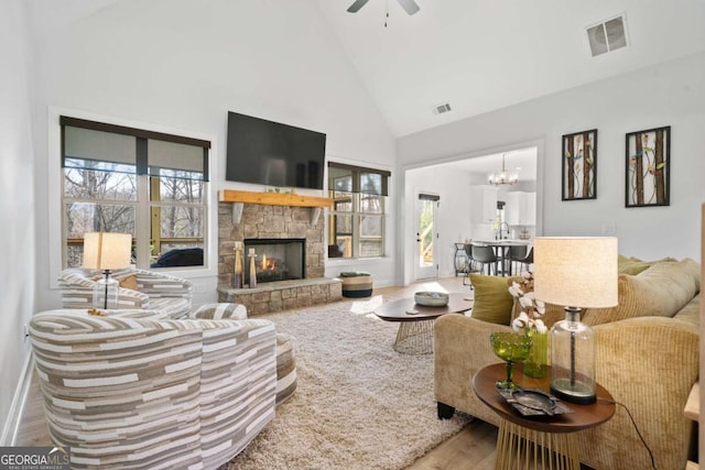 living area with a wealth of natural light, visible vents, a stone fireplace, and high vaulted ceiling