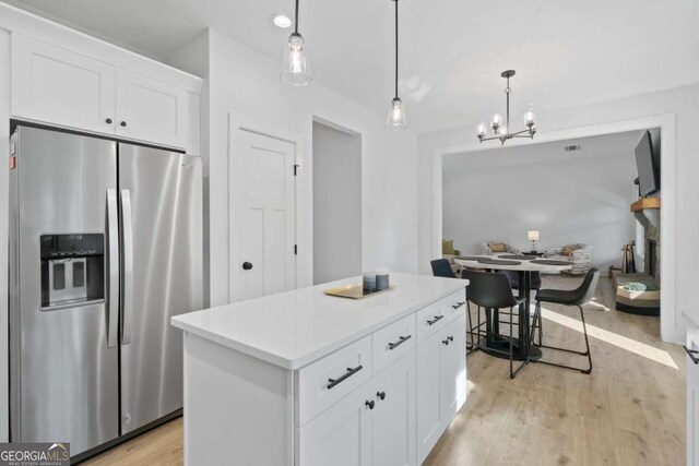 kitchen with stainless steel refrigerator with ice dispenser, a center island, light wood-style floors, white cabinets, and hanging light fixtures