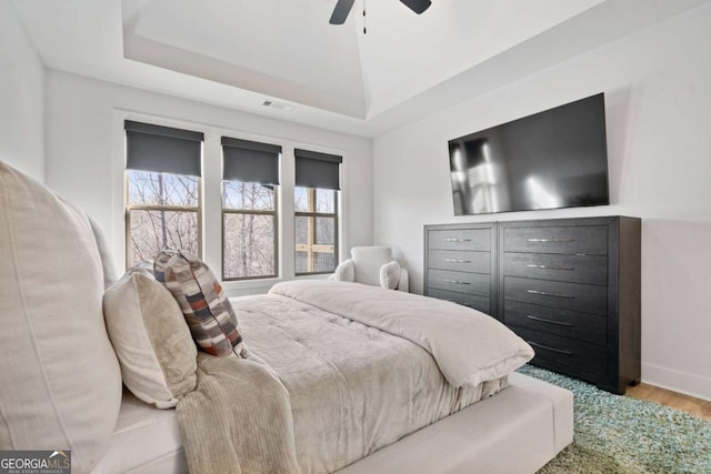 bedroom featuring visible vents, light wood-style flooring, baseboards, a raised ceiling, and ceiling fan