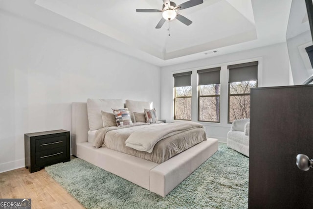 bedroom featuring visible vents, a raised ceiling, baseboards, and light wood finished floors