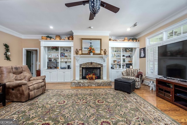 living room with ceiling fan, ornamental molding, wood-type flooring, and a stone fireplace