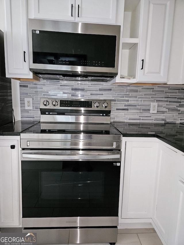 kitchen featuring stainless steel appliances, dark stone countertops, backsplash, and white cabinetry