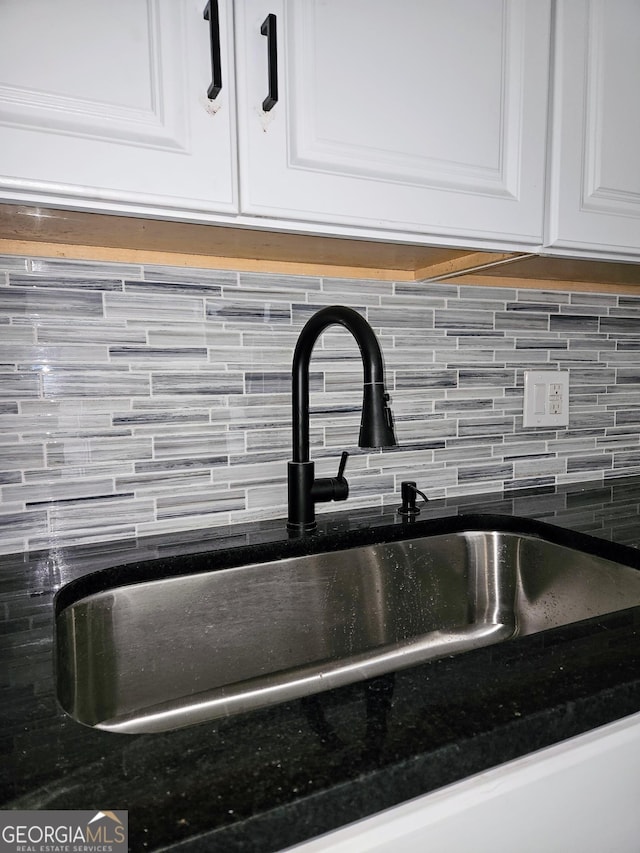 room details featuring sink, white cabinetry, dark stone countertops, and tasteful backsplash