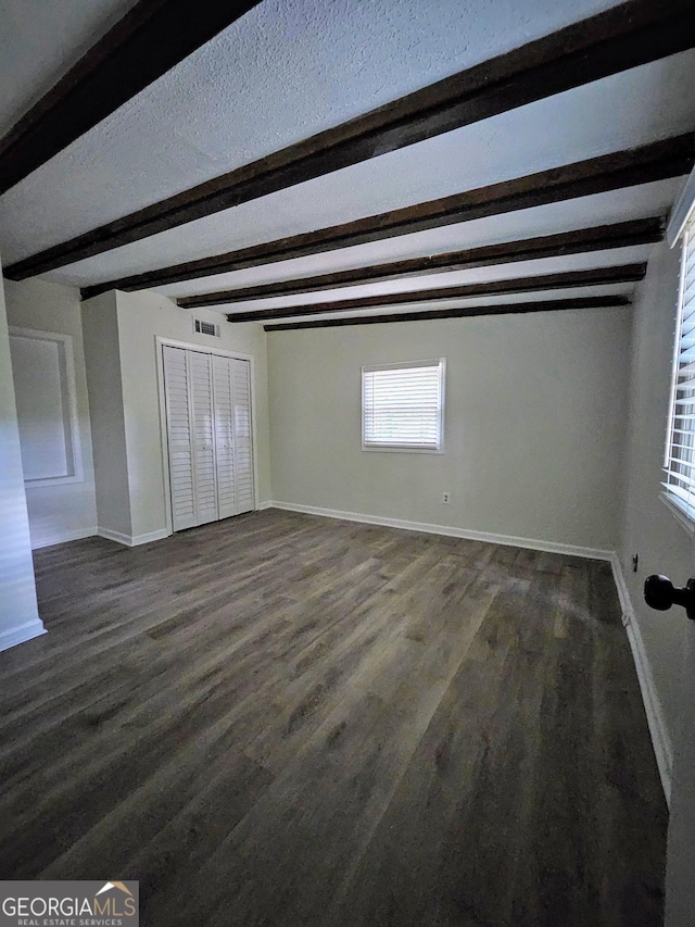 unfurnished bedroom featuring a textured ceiling, dark wood-type flooring, a closet, and beam ceiling