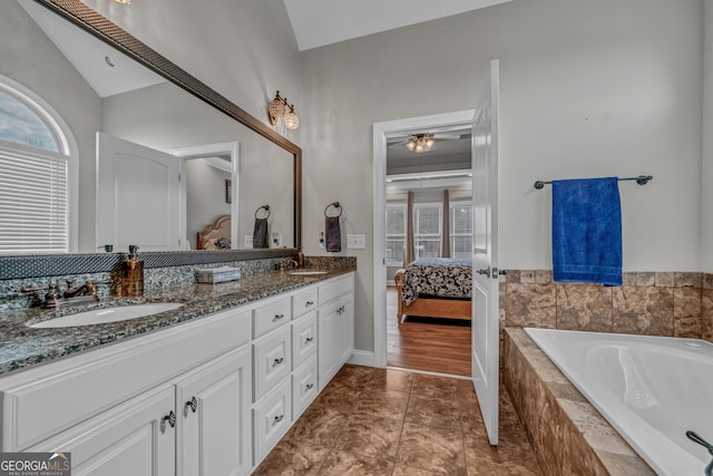 bathroom with lofted ceiling, ceiling fan, vanity, a relaxing tiled tub, and tile patterned floors