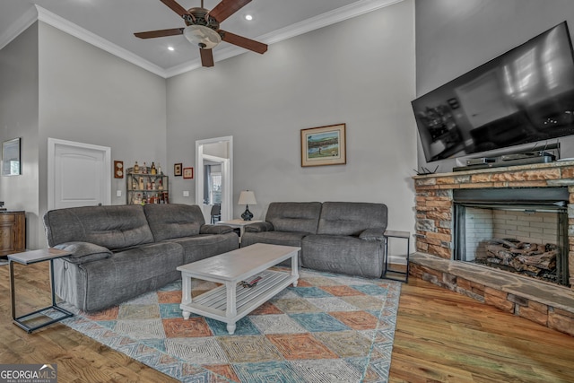 living room with ceiling fan, ornamental molding, a stone fireplace, and wood-type flooring