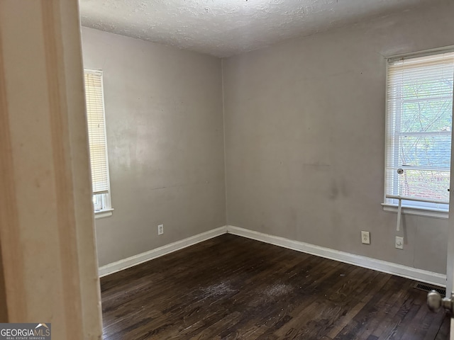 spare room featuring a textured ceiling, dark hardwood / wood-style floors, and a wealth of natural light