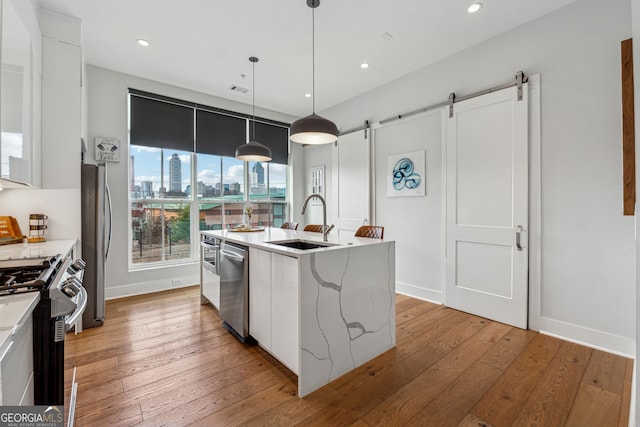 kitchen with pendant lighting, stainless steel appliances, an island with sink, and white cabinets