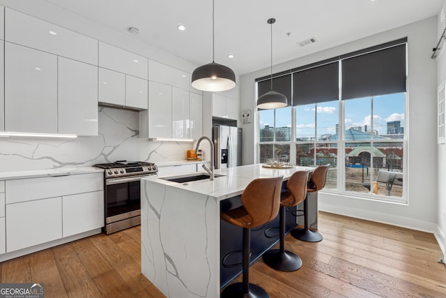 kitchen with a city view, a center island with sink, stainless steel appliances, a sink, and modern cabinets