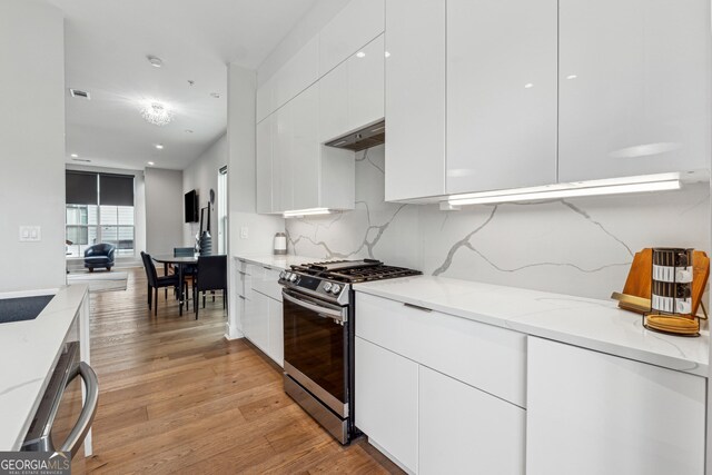 kitchen featuring stainless steel gas range oven, light hardwood / wood-style flooring, light stone countertops, decorative backsplash, and white cabinets