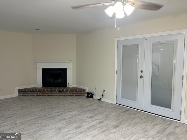 unfurnished living room featuring french doors, a fireplace, a ceiling fan, wood finished floors, and baseboards