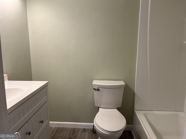 bathroom featuring a tub to relax in, toilet, wood finished floors, vanity, and baseboards