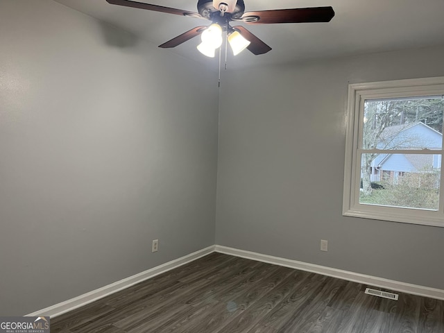 empty room featuring dark wood-style floors, plenty of natural light, visible vents, and baseboards