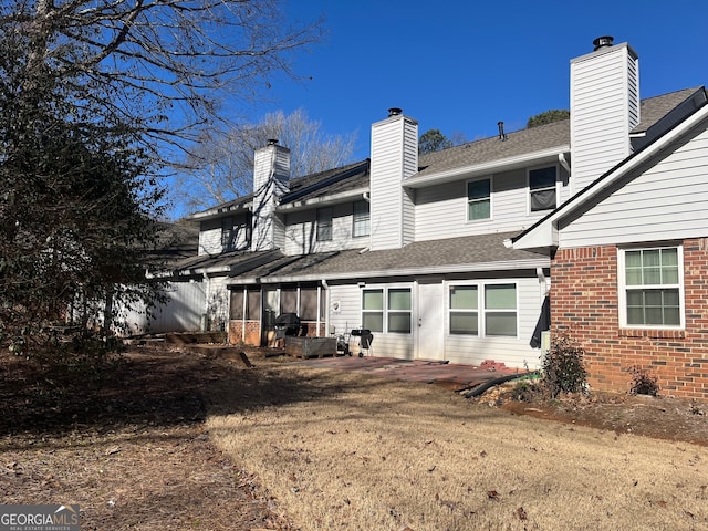 rear view of property with brick siding, a chimney, a shingled roof, and a sunroom