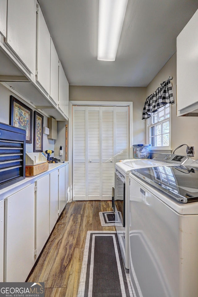 clothes washing area featuring cabinets, wood-type flooring, and washer and clothes dryer