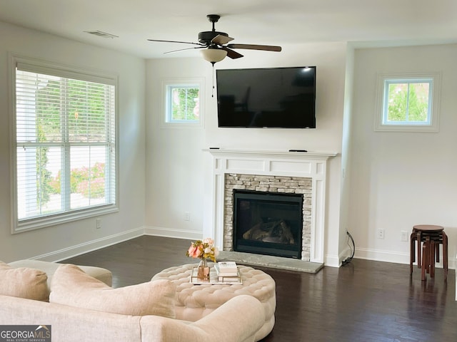 living room with ceiling fan, dark hardwood / wood-style flooring, and a stone fireplace